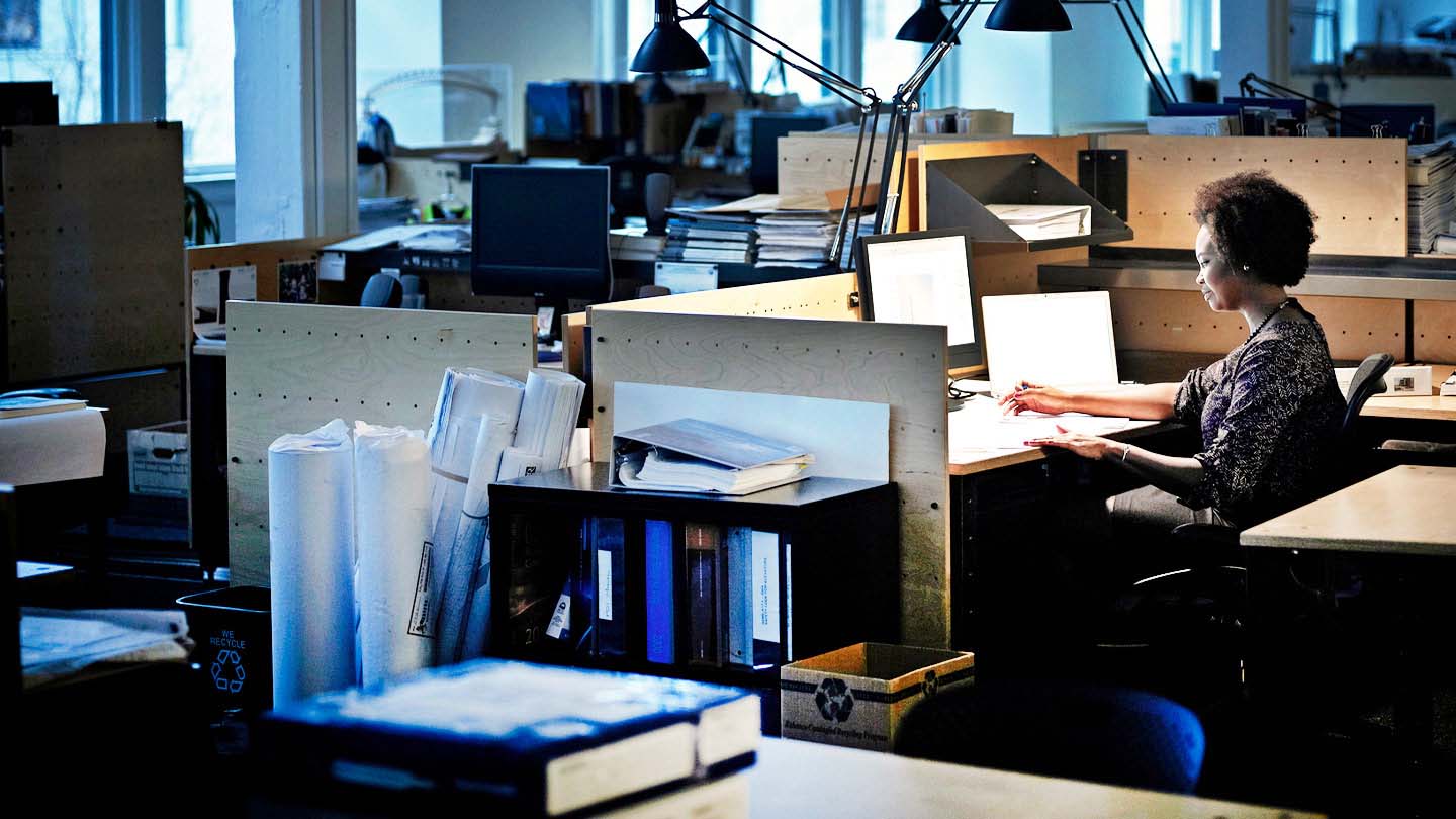 A woman looks over blueprints at her desk in an office setting